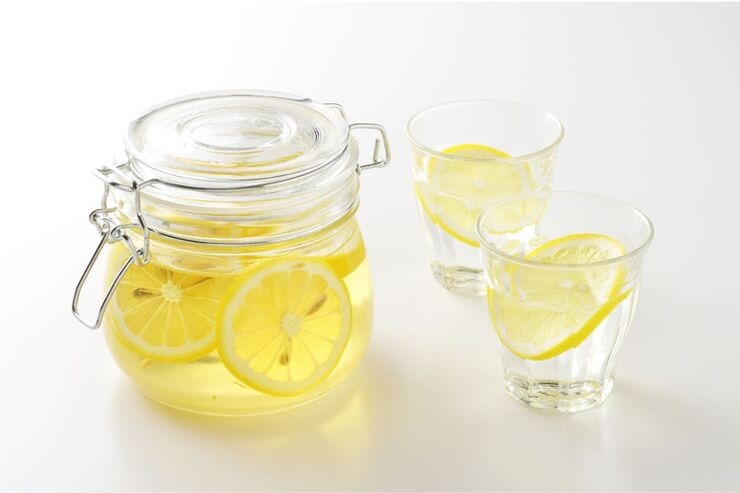 Barattolo con limone in liquido trasparente e due bicchieri con lo stesso contenuto 