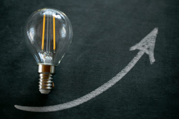 Lampadina sopra ad una superfice d'ardesia e freccia in salita disegnata con il gesso
