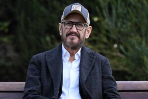 Marco Giallini con il berretto seduto su una panchina