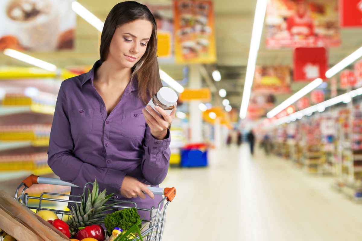 Donna al supermercato con il carrello che guarda un barattolo