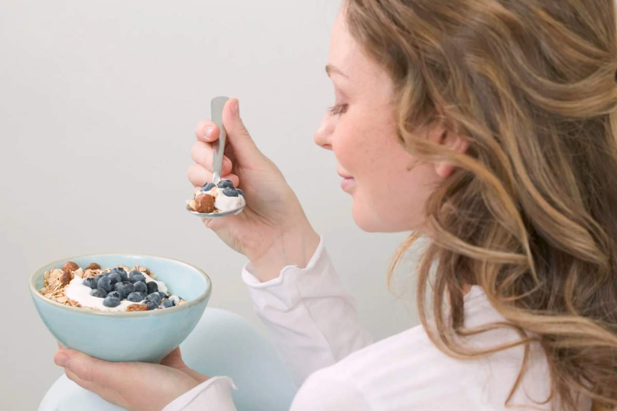 Donna che mangia mirtilli e cereali da una ciotola
