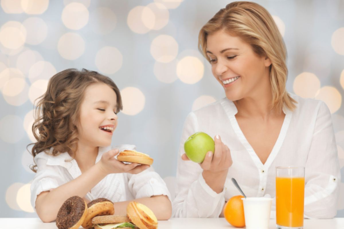 mamma che porge una mela alla bambina e bambina le porge un dolce
