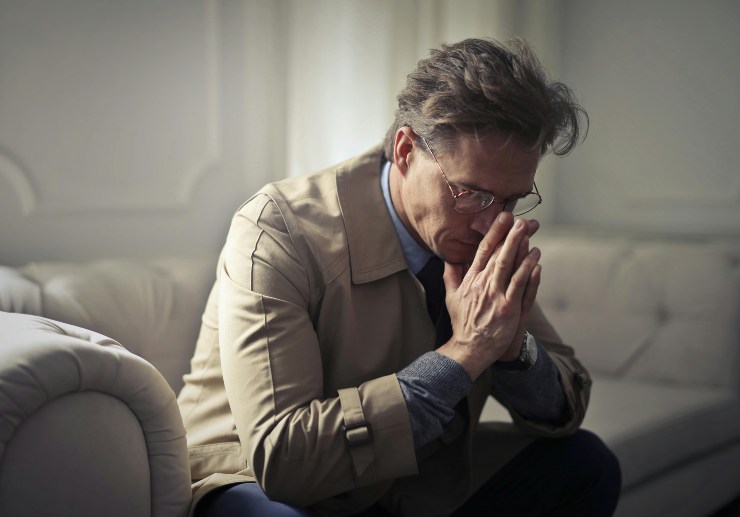uomo seduto sul divano con le mani congiunte davanti al viso